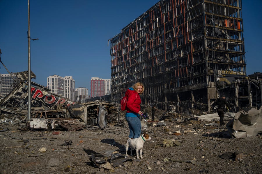 March 21, 2022:  Irina Zubchenko walks with her dog Max amid the destruction caused after shelling of a shopping center, in Kyiv, Ukraine.