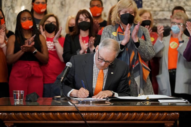 Washington Gov. Jay Inslee signs a bill that bans the manufacture, distribution and sale of firearm magazines that hold more than 10 rounds of ammunition in Washington state, Wednesday, March 23, 2022, at the Capitol in Olympia, Wash., as his wife Trudi, center-right, and other supporters applaud.