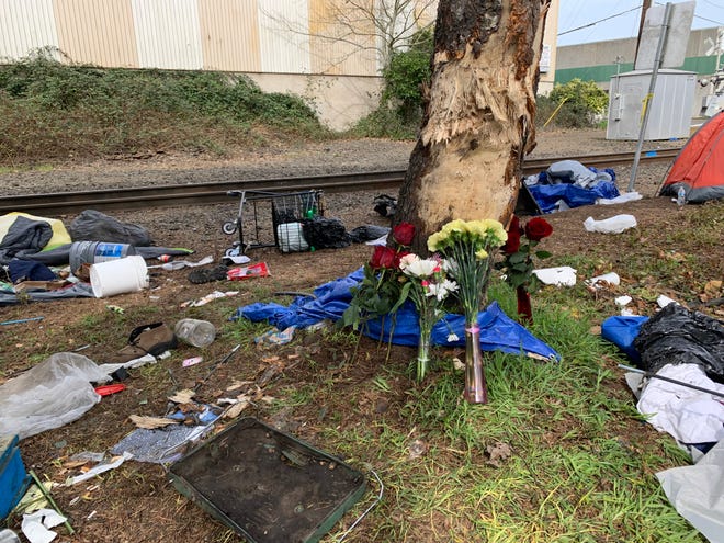 Flowers placed under a tree at a homeless camp off Front Street NE west of downtown Salem in memory of four people who died when a vehicle crashed into the site early Sunday, March 27, 2022.