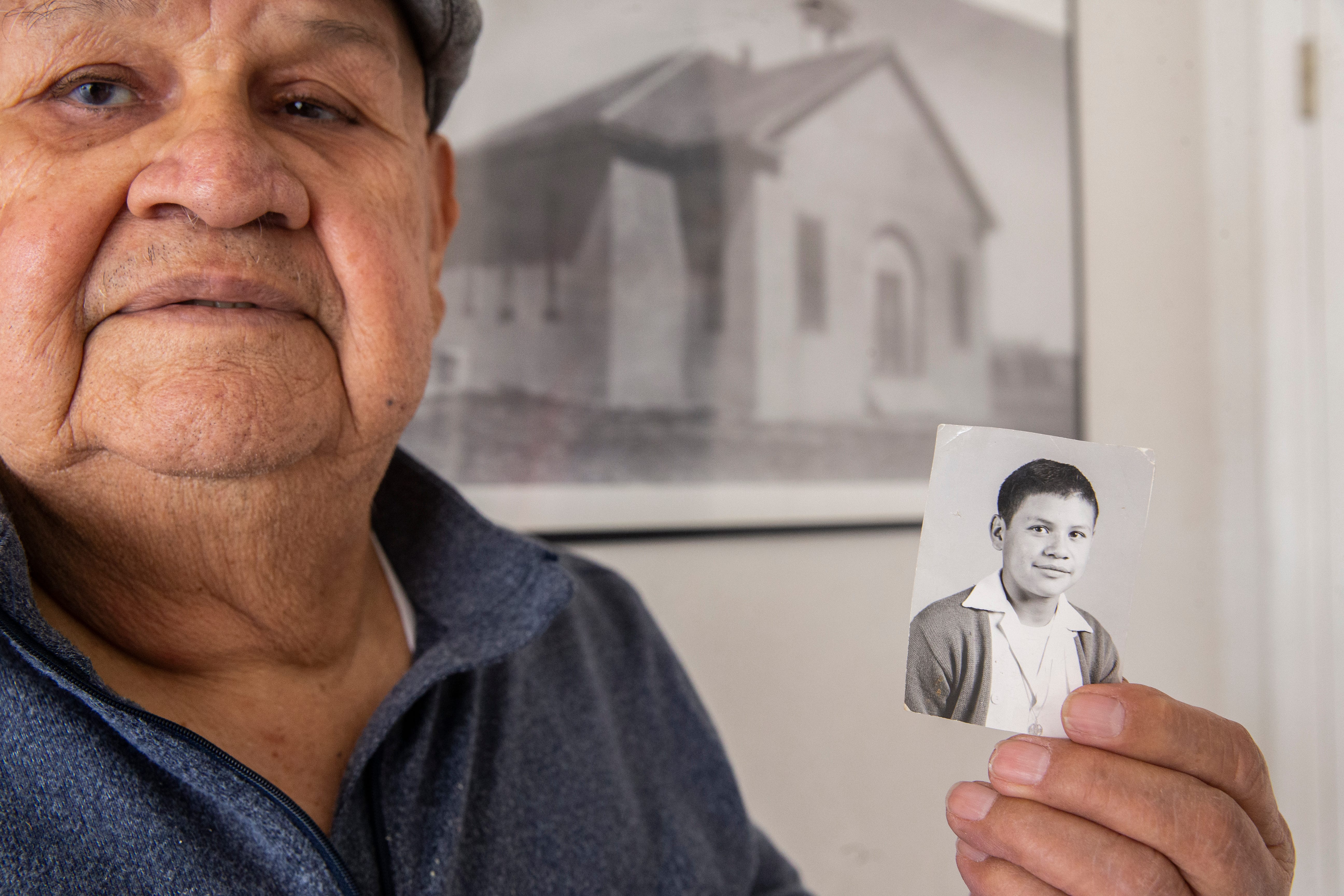 Joe Cabezuela holds an image of himself as a young child with a historic photo of Blackwell Elementary behind him at his home in El Paso, Texas.