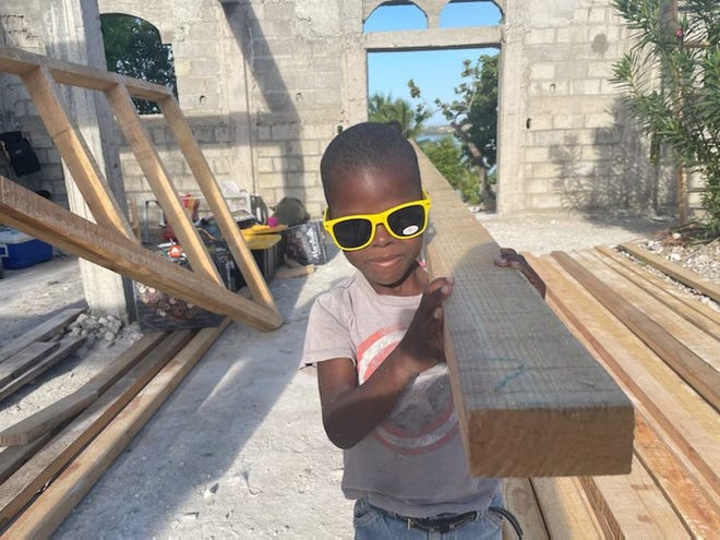 A youth wearing a T-shirt with the Captain America shield and sunglasses helps carry a board at the church work site in Bedzimel, Haiti.