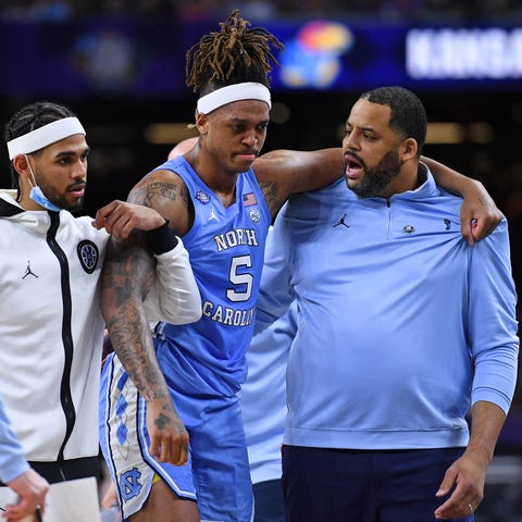 Armando Bacot is helped off the court by assistant