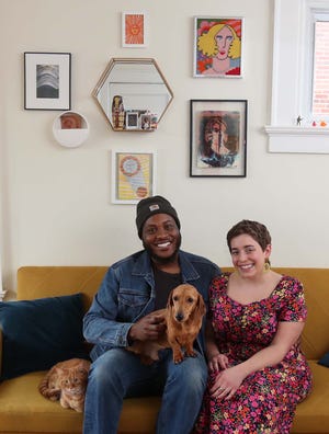 Chris Harvey, left, and his girlfriend Jess Fijalkovich started the bARTer NEO Instagram account for artists to exchange their work. Some examples of exchanged work are hanging on the wall behind them along with purchased pieces as they sit with their pets Goldie, left, and Peapod.