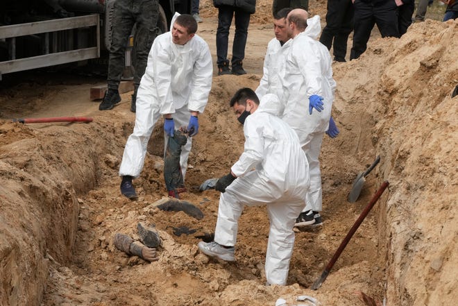 Men wearing protective gear exhume the bodies of killed civilians in Bucha, on the outskirts of Kyiv, Ukraine, Friday, April 8, 2022.