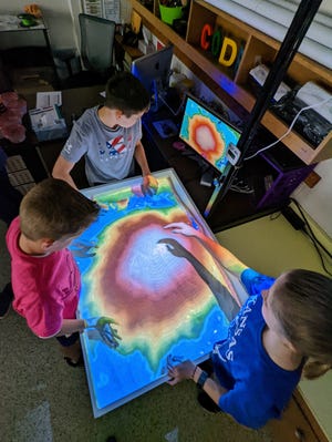 Clockwise from left, fifth-graders Kaeson Kruger, Logan Keen and Rylin Kirkwood look at a computer monitor to see the topography of the sand mountain they're creating.