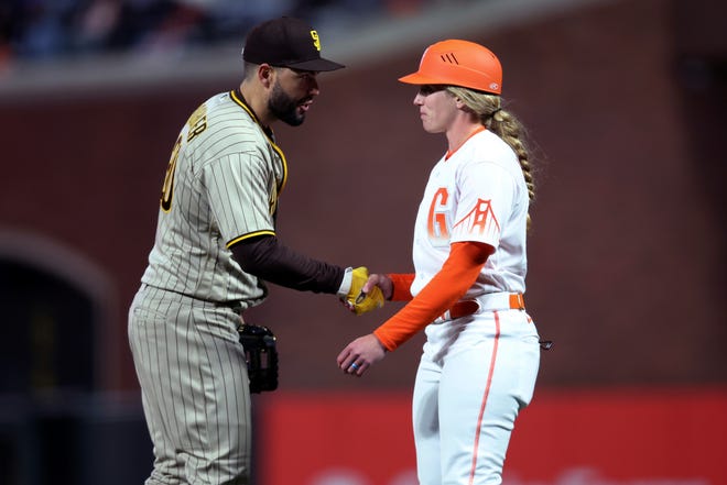 San Diego Padres first baseman Eric Hosmer, left, shakes hands with San Francisco Giants first base coach Alyssa Nakken during the third inning of a baseball game in San Francisco, Tuesday, April 12, 2022.