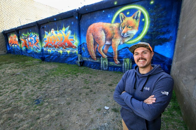 L'artiste local et peintre mural Brady Scott se tient à côté de la toute nouvelle fresque que lui et ses amis ont créée le long de South Main Street, vue de l'allée le mardi 12 avril 2022, à Hutchinson.  Scott a créé le renard et ses amis ont créé les sections graffiti street art de la peinture murale.