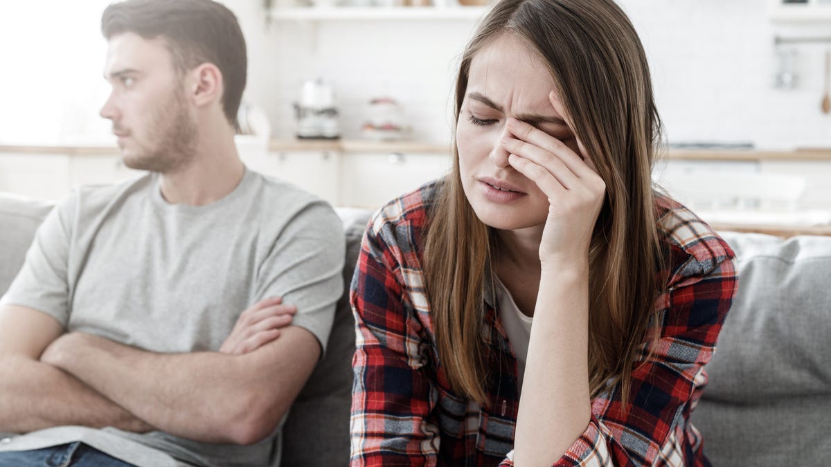 Couple conflict. Stressed crying female sitting on couch with abusive husband after quarrel, ready to divorce
