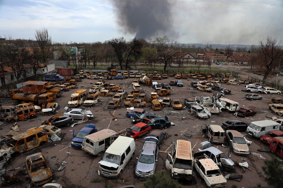 Damaged and burned vehicles are seen at a destroyed part of the Illich Iron & Steel Works Metallurgical Plant, as smoke rises from the Metallurgical Combine Azovstal during heavy fighting, in an area controlled by Russian-backed separatist forces in Mariupol, Ukraine, Monday, April 18, 2022. Mariupol, a strategic port on the Sea of Azov, has been besieged by Russian troops and forces from self-proclaimed separatist areas in eastern Ukraine for more than six weeks.