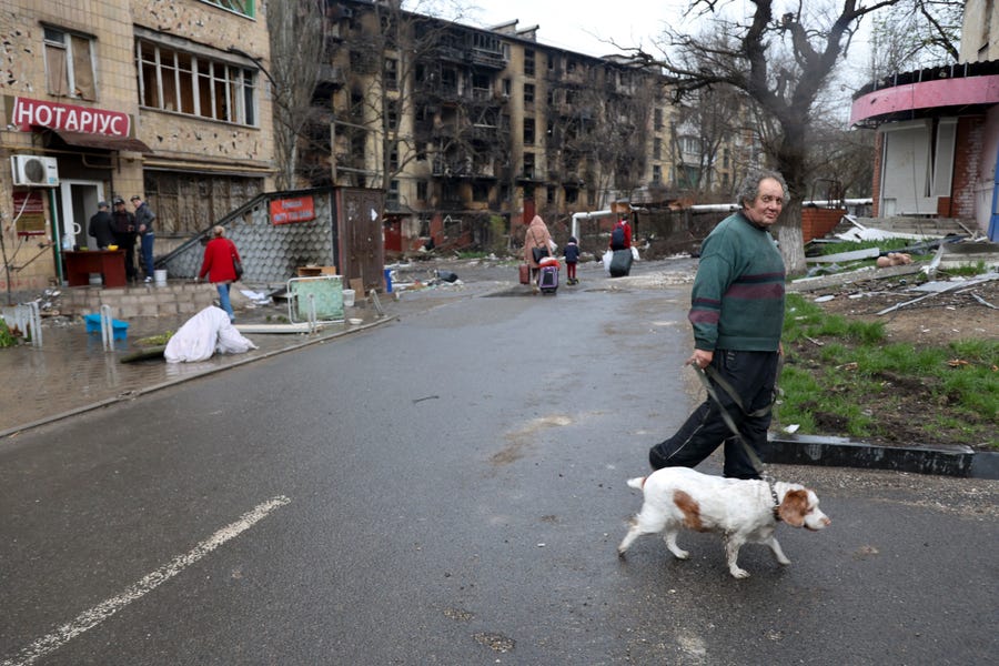 A man with a dog walks in a street along damaged during a heavy fighting apartment buildings in an area controlled by Russian-backed separatist forces in Mariupol, Ukraine, Tuesday, April 19, 2022.