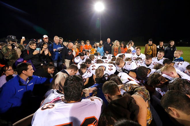 FILE - Bremerton assistant football coach Joe Kennedy, obscured at center in blue, is surrounded by Centralia High School football players as they kneel and pray with him on the field after their game against Bremerton on Oct. 16, 2015, in Bremerton, Wash. After losing his coaching job for refusing to stop kneeling in prayer with players and spectators on the field immediately after football games, Kennedy will take his arguments before the U.S. Supreme Court on Monday, April 25, 2022, saying the Bremerton School District violated his First Amendment rights by refusing to let him continue praying at midfield after games. (Meegan M. Reid/Kitsap Sun via AP, File)