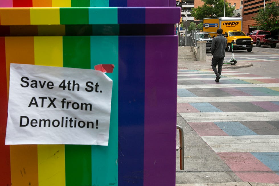 A pedestrian walks across a rainbow walkway on Thursday, where a sign posted on West Fourth Street urges people to take action against demolition plans for the block.