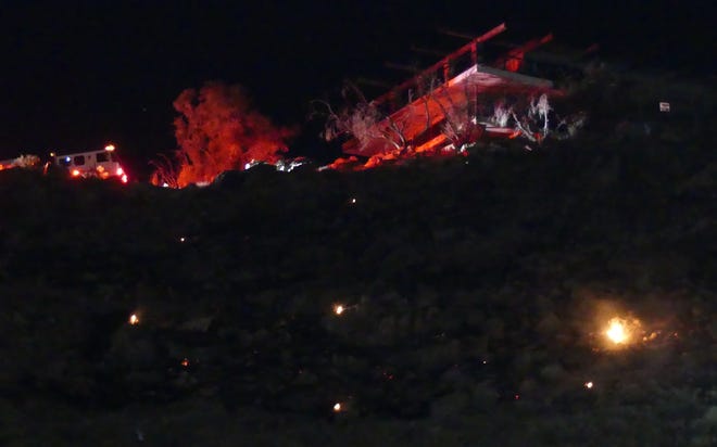 Fire engine lights illuminate the iconic Hilltop house on Friday night as firefighters below work to extinguish a vegetation fire on the rocky hillside between the house and Walmart in Apple Valley.