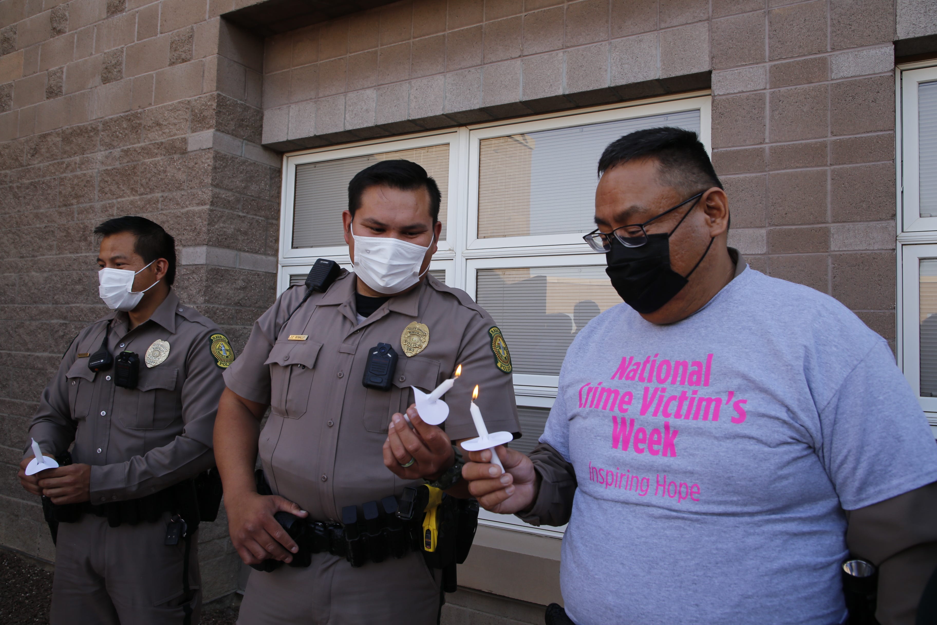 Navajo Police Officer Terrence Benally, center, and Navajo Police Capt. Leonard Redhorse III help each other light candles during the candlelight vigil to observe National Crime Victims' Rights Week on April 27, 2022 at Northern Navajo Medical Center in Shiprock, New Mexico.