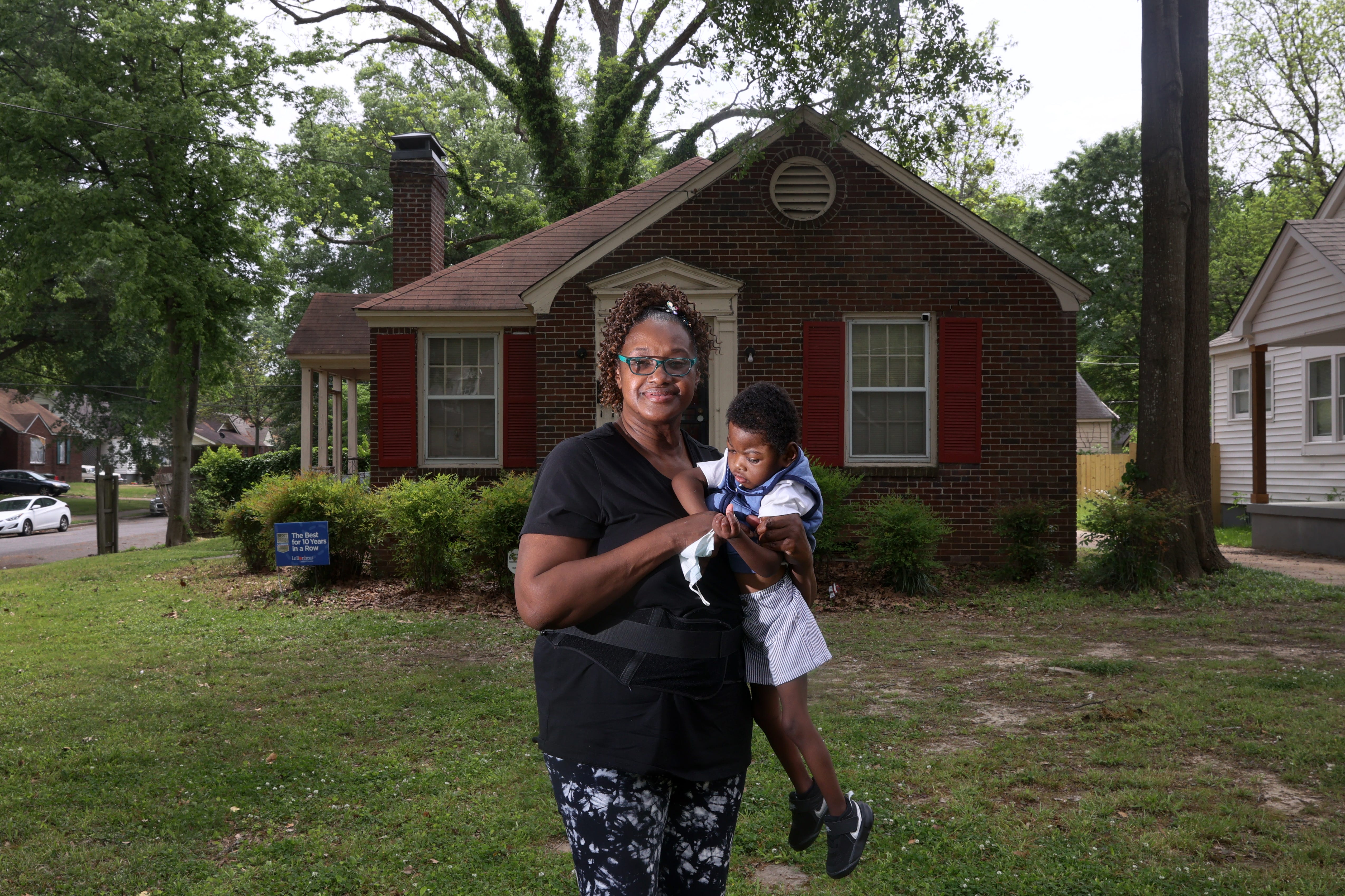 A grandmother holds her grandson while standing outside their home.