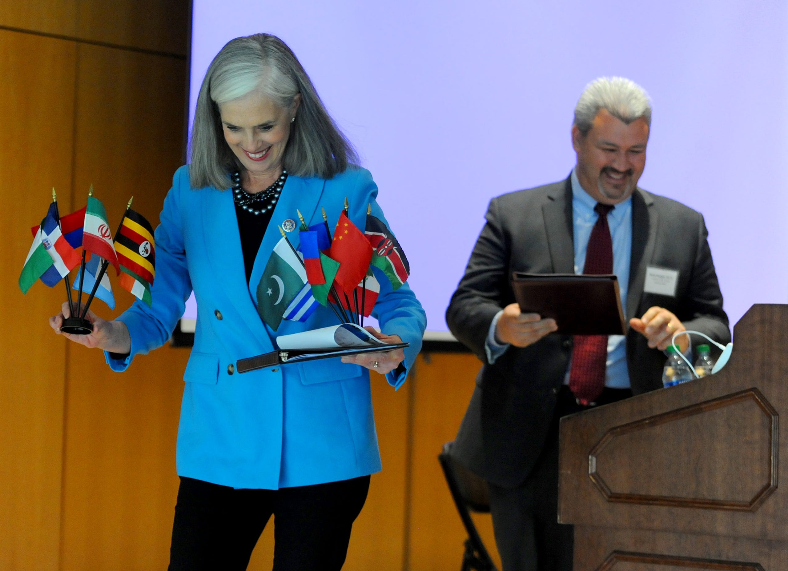 Rep. Katherine Clark, Assistant House Speaker, leaves the stage with flags given to her by students after she announced a $600,000 expansion of the MetroWest Scholars Early Start program, early college funding for Waltham students,  at Framingham State University, May 3, 2022.  At right is Waltham Supt. of Schools Brian Reagan.
