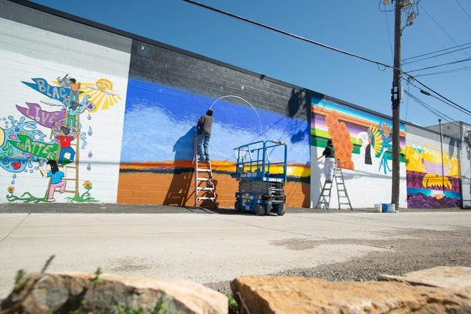 The west-facing wall to the Habitat for Humanity ReStore, 121 N.E. Gordon St., has a new color palette as artists George Mayfield, left, Jaime Colón, right, and Mona Cliff (not pictured) create the multicultural mural on April 14.