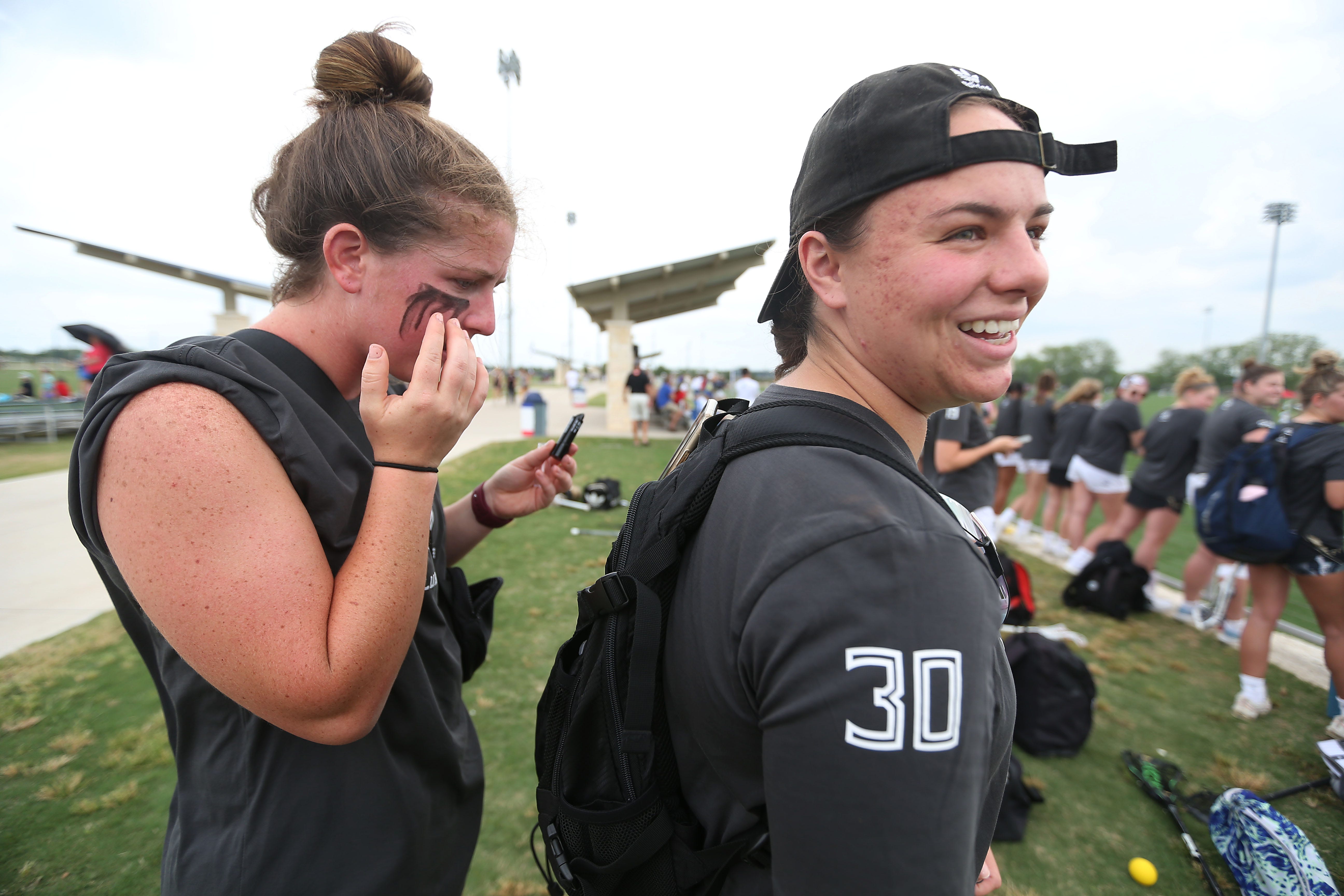 Florida State lacrosse player Erica Simkins, left, rests her phone on Sophia Villalonga's backpack so she can apply eye black before they warm up for the game against BYU in the WCLA National Championships Wednesday, May 4, 2022, in Round Rock, Texas.