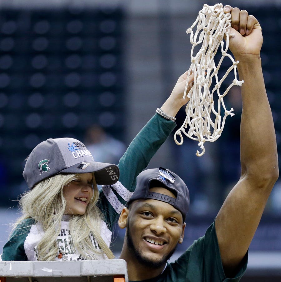 Michigan State forward Adreian Payne hoists a basketball hoop net in one arm and Lacey Holsworth in the other after Michigan State defeated Michigan 69-55 in an NCAA college game March 16, 2014, in the championship of the Big Ten Conference tournament in Indianapolis.