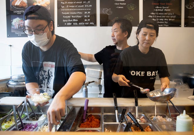 Paul and Priscilla Song, right, and employee Benjamin Suh, left, serve customers Poke Bay on Wednesday. The Songs announced that at the end of the month they are closing the restaurant they have run since 2017. The building they occupy was bought by the University of Texas.