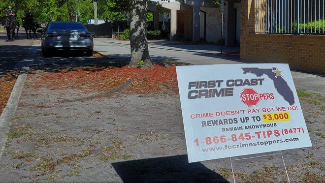 A First Coast Crime Stoppers sign marks the spot on West 28th Street where a 17-year-old boy was shot Wednesday afternoon outside Andrew Jackson High School. The Sheriff's Office mounted patrol, left, were called in Thursday for extra security.