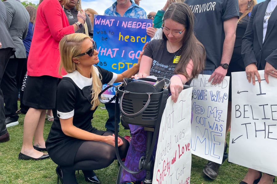 Paris Hilton, left kneeling, talking with Sasha Oates, right, from Sacramento, Calif., after speaking at a Stop Institutional Child Abuse event, Wednesday, May 11, 2022 in Washington.