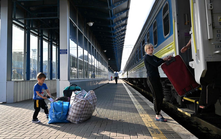 A woman and her child, one of the thousands of women and children who fled the Ukraine after Russia invaded, disembarks with her luggage upon their arrival from Poland, at Kyiv's railway station on May 12, 2022.