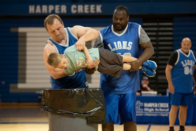 Former Detroit Lions players Cory Schlesinger and Scott Conover pretend to throw 6-year-old Remington Klingaman in the trash at Harper Creek High School on Tuesday, May 17, 2022.