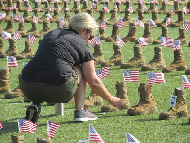 Anna Waggoner volunteers to place flags and name tags on boots Friday, May 20, 2022, at Hedrick Stadium on Fort Bragg. The boots will be on display for Saturday's  Run, Honor, Remember 5K to honor service members who have died since 9/11.