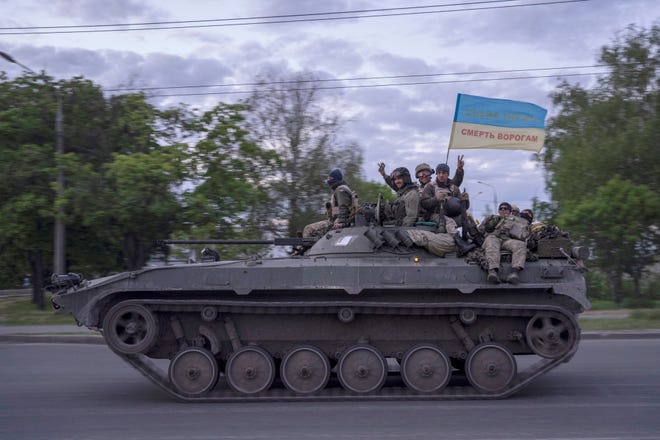 Ukrainian serviceman wave a flag with writing reading in Ukrainian "Glory to Ukraine", top, and "Death to the enemies" as they ride atop a tank in the Kharkiv region, eastern Ukraine, Monday, May 16, 2022.