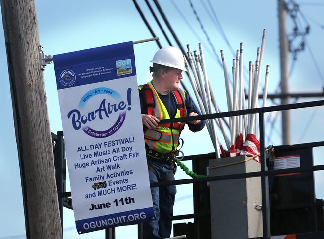 Ogunquit Public Works crew member Ritchie Hall hangs a flag on Route 1, advertising the town's upcoming BonAire! and Pride events.