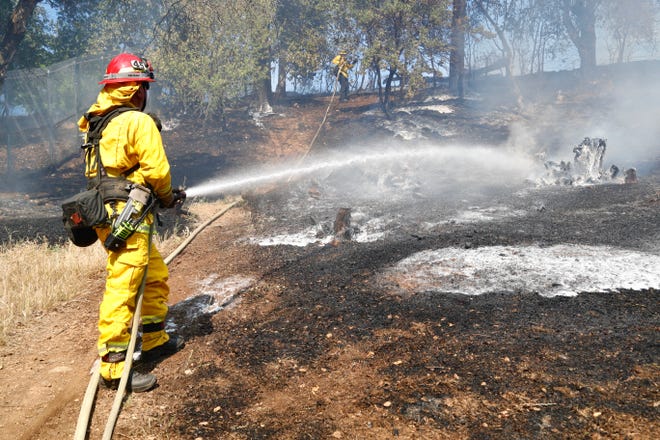 Redding firefighters hose down a field that burned behind the Showboat Lounge on Hartnell Avenue, just south of Cypress Avenue, on Wednesday afternoon, May 25, 2022.