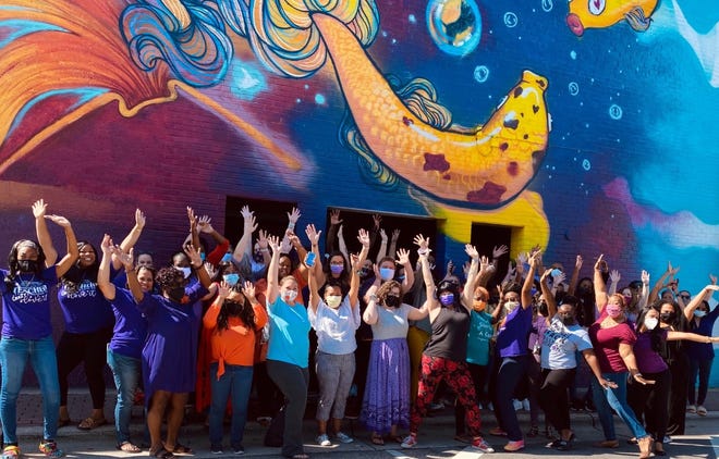 Staff members at The Capitol Encore Academy in downtown Fayetteville stand in front of a mural on the back of the school in August 2021.