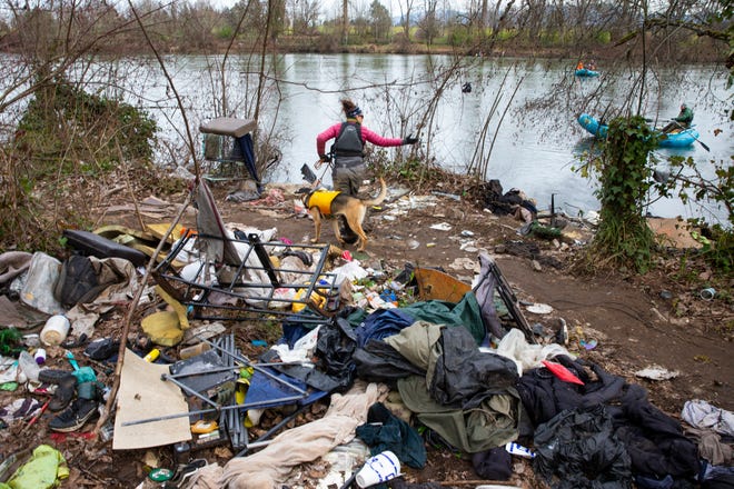 Michelle Emmons with Willamette Riverkeeper calls to Roger Bailey in a raft at right as she and her dog Ranger walk through an area of garbage left behind along the Willamette River bank west of the Whilamut Passage Bridge in Eugene.