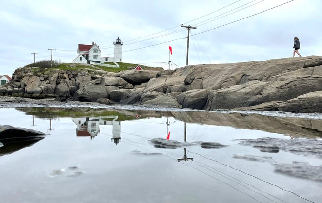 Nubble Lighthouse is reflected in a puddle of water on the rocks on an overcast afternoon in York.