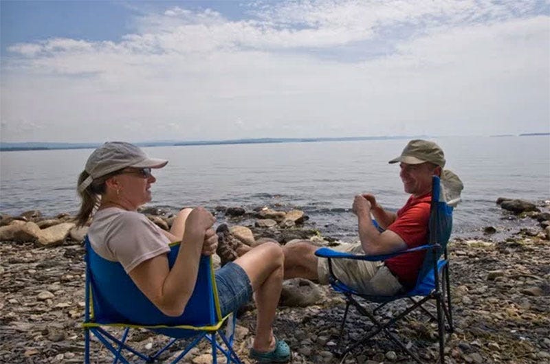 A man and a woman sit in folding camp chairs on the shores of Lake Champlain