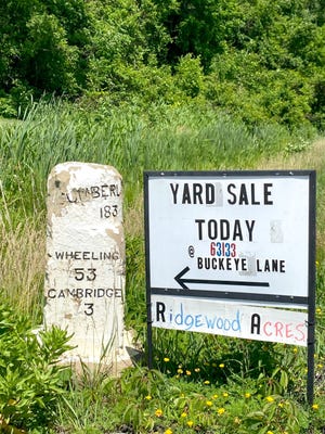 A yard sale sign along U.S. Route 40 in Cambridge is placed strategically close to one of the original national road markers. The four-day-long yard sale event spans from Illinois to Maryland and offers visitors a chance to explore the National Road and find hidden treasures along the way.