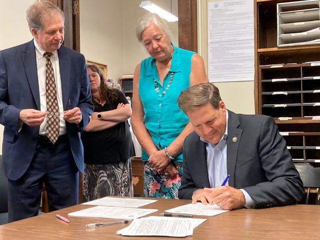 New Hampshire Gov. Chris Sununu signs papers to file for reelection, Friday, June 10, 2022, at the secretary of state's office in Concord. Sununu is accompanied by Secretary of State David Scanlan, far left, and staffers Kaley Dion, background, and Karen Ladd.