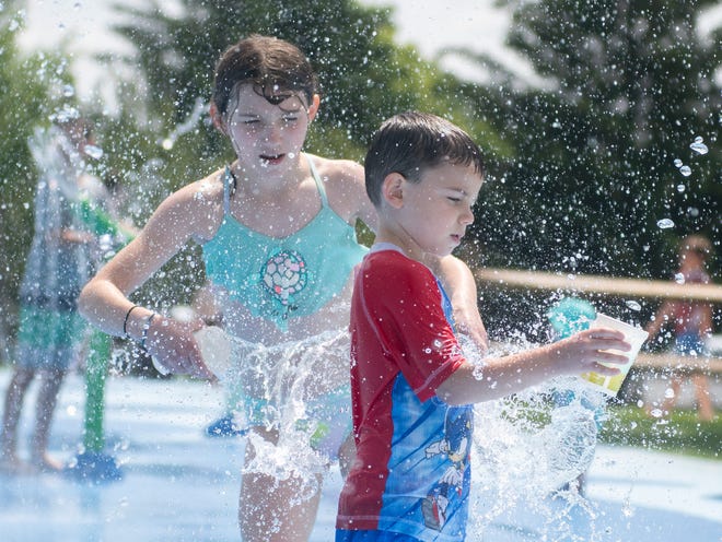 Natalie Mounts, 10, sneaks up on her brother, Travis Mounts, 5, and tosses a cup of water as he refills his cup Tuesday during a sibling water fight at Aurora's Kiwanis-Moore Park splash pad.