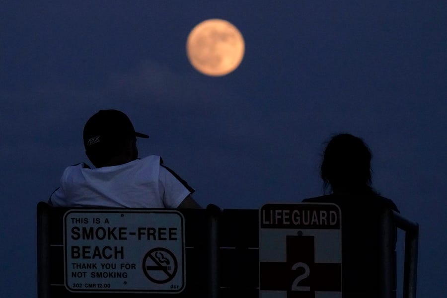 People watch the rising moon Monday, June 13, 2022, in East Boston, Mass. The moon will reach its full stage on Tuesday, during a phenomenon known as a supermoon because of its proximity to Earth, and it is also labeled as the "Strawberry Moon" because it is the full moon at strawberry harvest time.