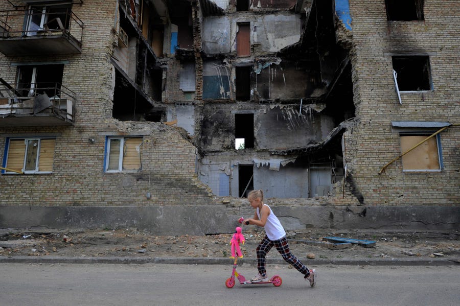A girl rides a kick scooter past a destroyed residential building in the village of Horenka, Kyiv region, on June 4, 2022 amid the Russian invasion of Ukraine.