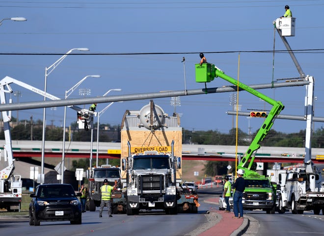 Bucket trucks and workmen loosen and lift traffic signal arms as traffic goes around a Rentech boiler being transported on a flatbed trailer Wednesday morning.