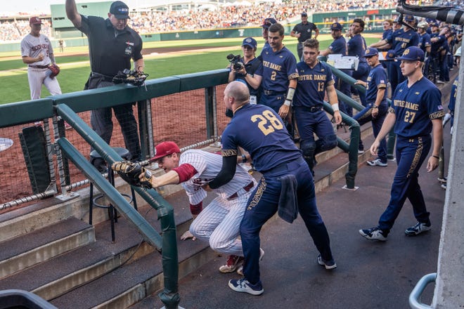 June 19, 2022; Omaha, NE, USA; Oklahoma Sooners first baseman Blake Robertson (26) is helped by Notre Dame Fighting Irish pitcher John Michael Bertrand (28) after falling into the dugout during the first inning at Charles Schwab Field. Mandatory Credit: Dylan Widger-USA TODAY Sports