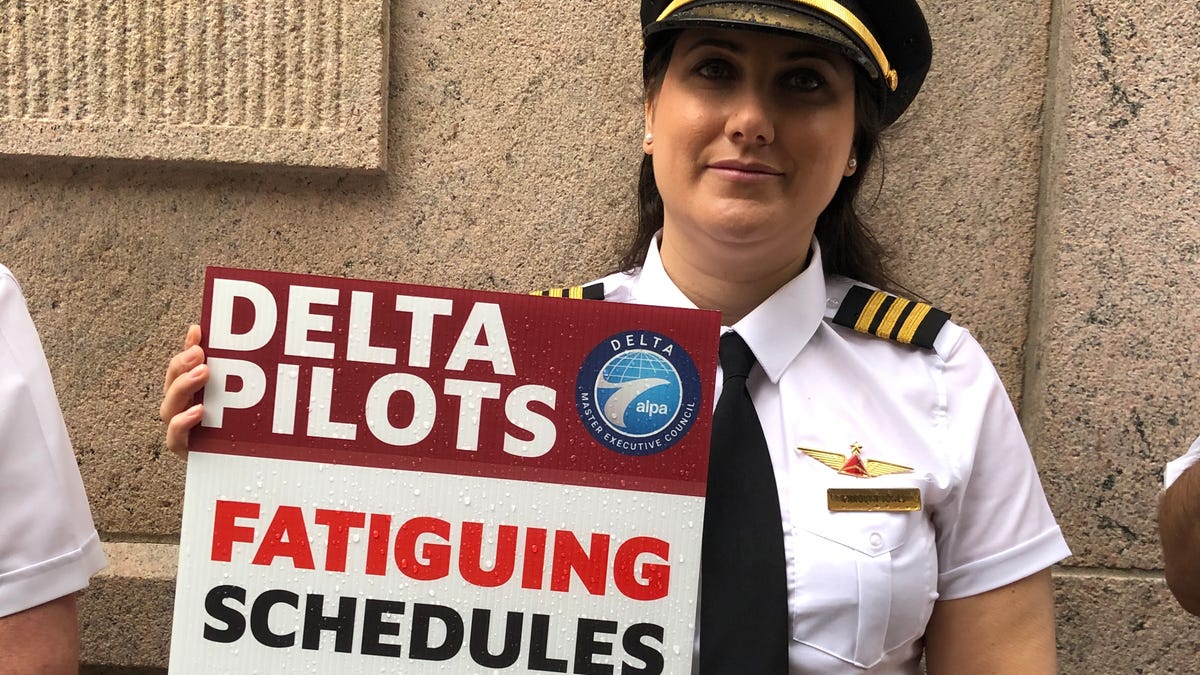 A Delta Air Lines pilot holding a sign that says "fatiguing schedules = poor reliability."