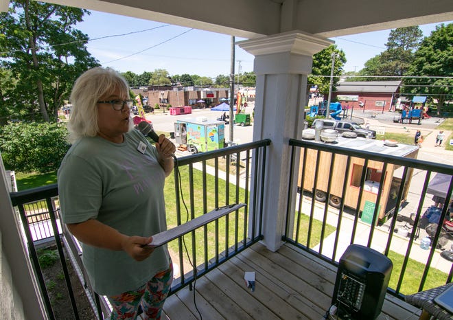 Susie Tennyson stands on the balcony of the Pinckney State Farm office facing the town square and announces the various food trucks offering food and drinks at Food Truck Friday in downtown Pinckney on Friday, June 24, 2022.