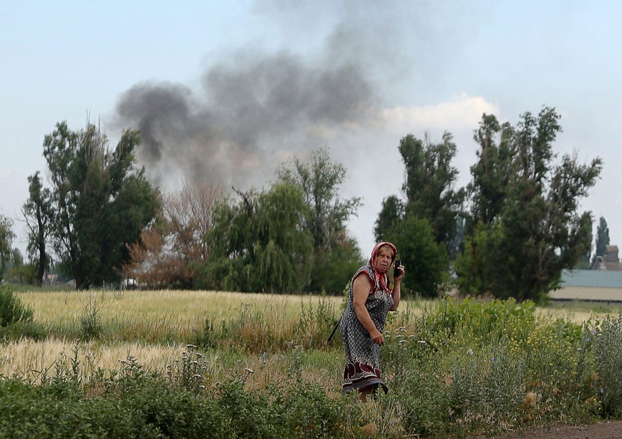 A woman speaks on a mobile phone on a roadside while smoke rises behind in the village Sviato-Pokrovske, Donetsk region, on June 23, 2022, amid Russia's military invasion launched on Ukraine.