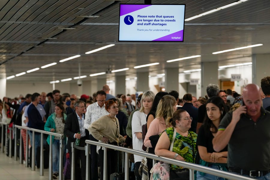 Travelers wait in long lines to check in and board flights at Amsterdam's Schiphol Airport, Netherlands, Tuesday, June 21, 2022.