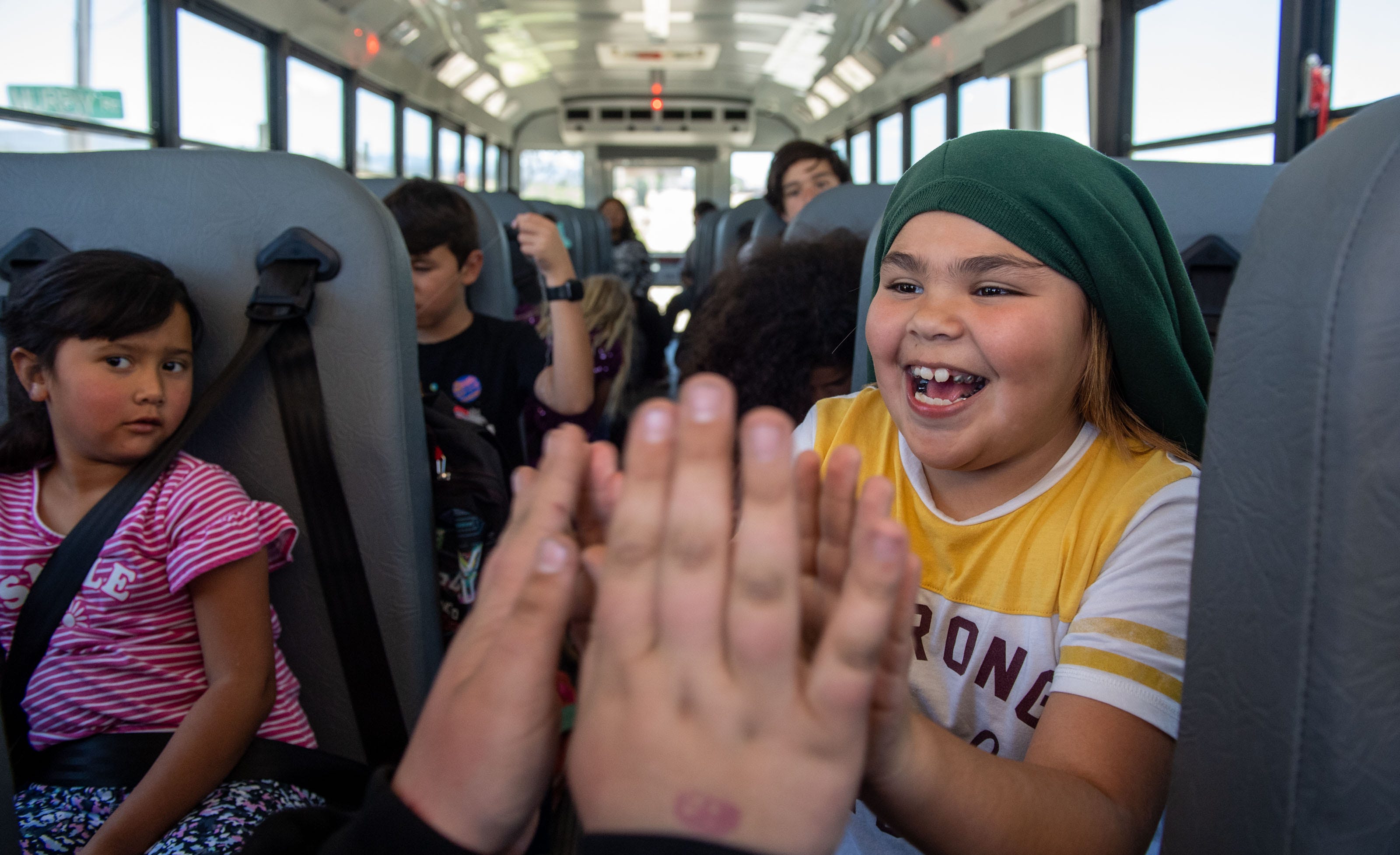 Paloma Segura, 7, plays pattycake with an older student as they ride the bus after school ends in Lockwood, Calif., on Wednesday, May 11, 2022. Segura is currently a 2nd grader at San Antonio Elementary School. 