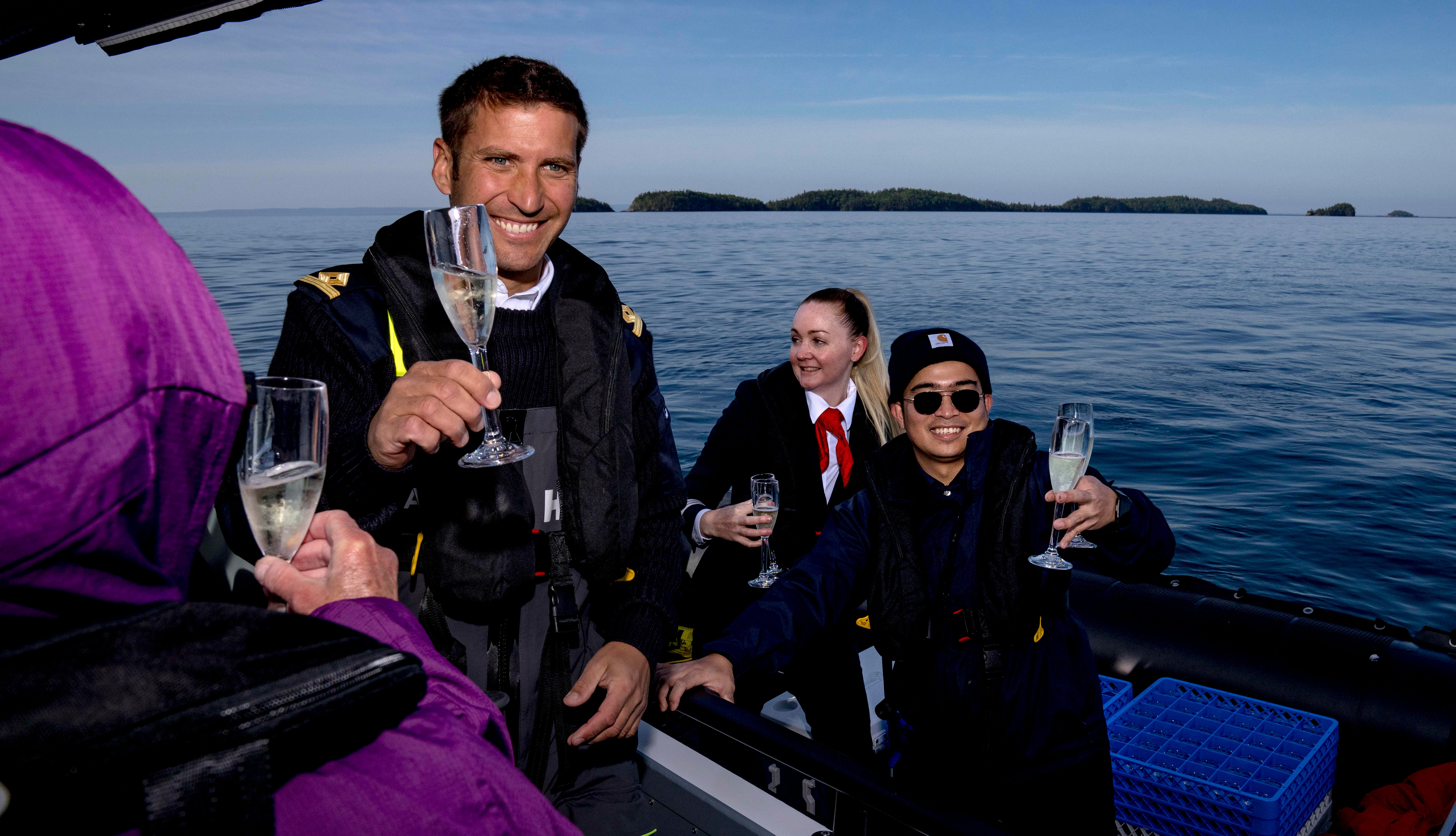Third officer Nikola Marinovic, left, beverage manager Tammy Marshall and crew member Darrell Ganoria raise champagne glasses in Silver Islet in Ontario, Canada, on June 24. The Special Operations Boat saw a Zodiac boat in the distance that looked stranded, and crew members surprised the passengers with glasses of champagne.