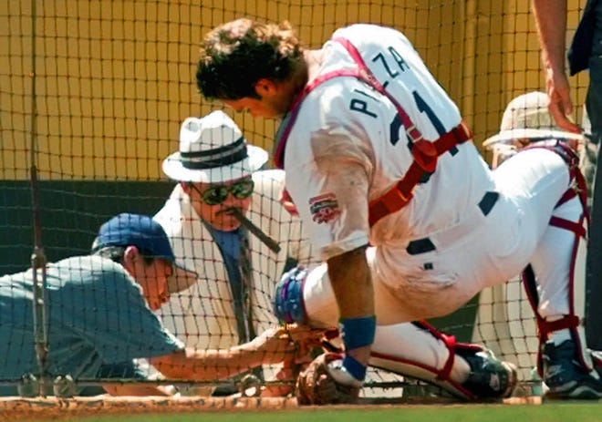 Los Angeles Dodgers' catcher Mike Piazza gets help from Dodgers scout Mike Brito, in white fedora, unhooking his protective gear from the fence after catching afoul ball off the bat of the Florida Marlins' Livan Hernandez on Sept. 6, 1997, at Dodger Stadium.